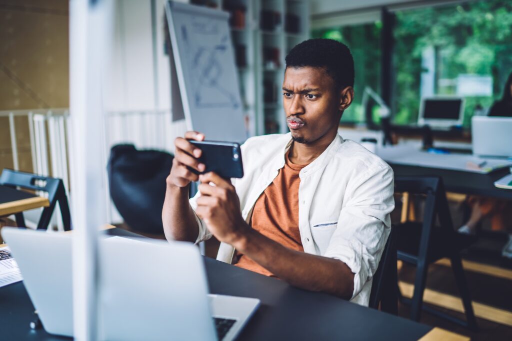 Dark skinned male student puzzled with web information on university website photographing laptop